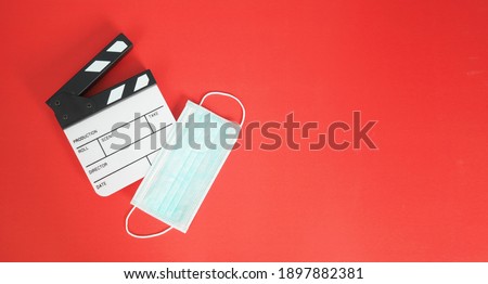 Small white Clapper board or  clapperboard or movie slate with face mask. it use in film,movies production and cinema industry on red background.Covid-19 or social distance concept.