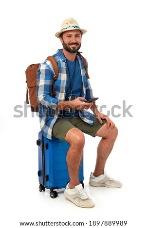 Cheerful traveler sitting on his suitcase with mobile phone