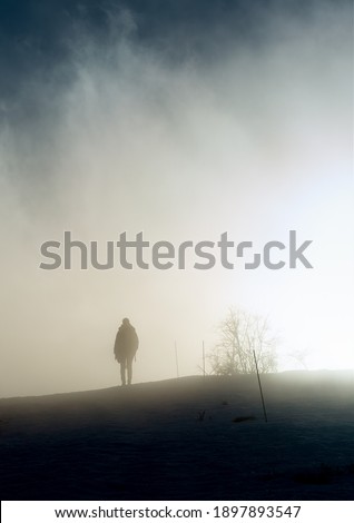 A woman walks towards the sun in the blown fog on top of a mountain on a cold winter day in south of France