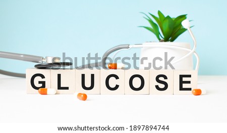 The word GLUCOSE is written on wooden cubes near a stethoscope on a wooden background. Medical concept