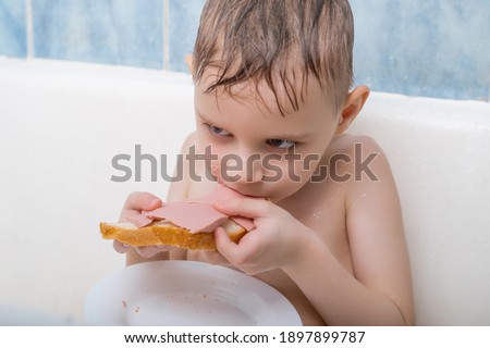 A young boy is eating in the bath. Snack in the bathroom.