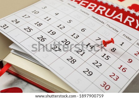 Calendar with marked Valentine's Day and notebooks on white marble table, closeup