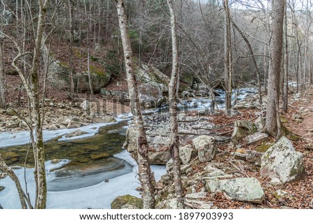 Frozen creek in the Laurel Snow state natural area in Dayton, Tennessee covered with snow and flowing underneath the ice along the trail in the woodlands on a bright day in wintertime Royalty-Free Stock Photo #1897903993
