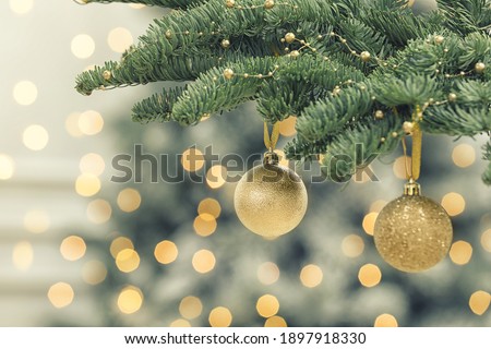 Golden Christmas balls hanging on fir tree against blurred festive lights
