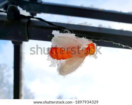 Part of a luminous garland in the form of plastic bees, wound on a black metal structure in the recreation area (gazebo), on a snowy cold winter day, icy and in the snow, against the blue sky