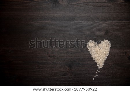 Rice grains are scattered on a dark wooden background in the shape of a heart
