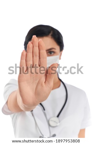 Professional doctor in medical protective mask standing isolated over white studio background and showing stop gesture. Concept of virus and diseases.