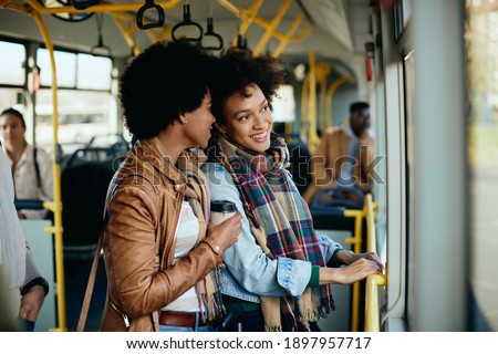 Happy black woman commuting with her female friend in a public transport.  Royalty-Free Stock Photo #1897957717