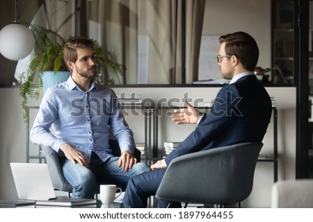 Colleagues businessmen discussing project strategy, sharing ideas, sitting in armchairs in modern office, business partners negotiating startup, hr manager holding interview with candidate Royalty-Free Stock Photo #1897964455