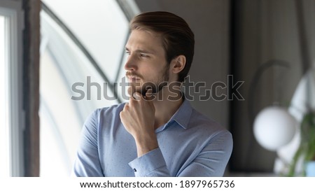 Close up thoughtful dreamy businessman touching chin, pondering strategy, pensive entrepreneur executive standing in modern office, looking to aside, dreaming about new opportunities, planning