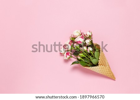 Small roses in waffle cone on pink background, copy space. Minimal style flat lay. For greeting card, invitation. March 8, February 14, birthday, Valentine's, Mother's, Women's day concept. Top view.