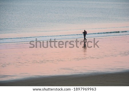 A lone tourist with a backpack shoots a wonderful Arctic sunset landscape on the ocean. Russia. 