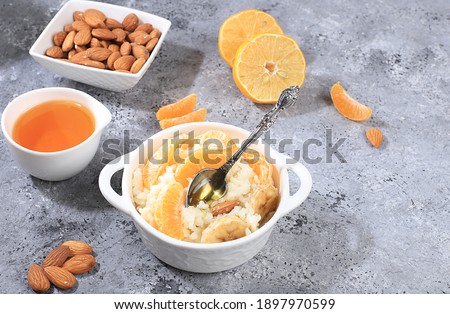 Useful breakfast with ingredients, flat lay, rice pudding with bananas, honey, tangerines and almonds on a sunny table. Healthy and natural food concept, lifestyle, food for children, selective focus