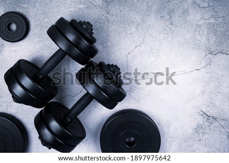 Top view of black dumbbells and different weight plates on gray textured background. Flat lay. Fitness or bodybuilding sport training concept. Copy space.