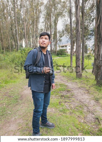 Young man walking in the woods. With his backpack and cell phone recording and taking pictures.