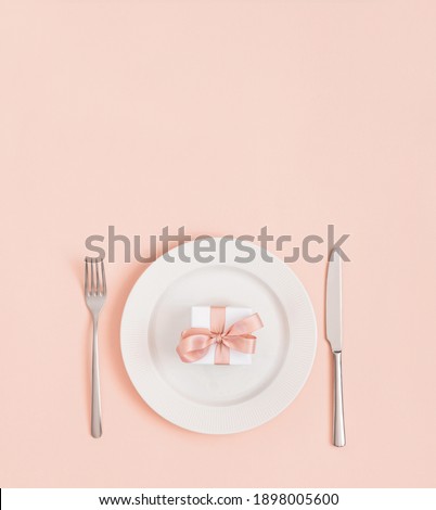 Festive table setting for Valentines Day, Mothers Day, Birthday or Christmas. Gift in a plate on a pastel pink background. Minimal concept. Space for text. Top view, flat lay. Vertical orientation.
