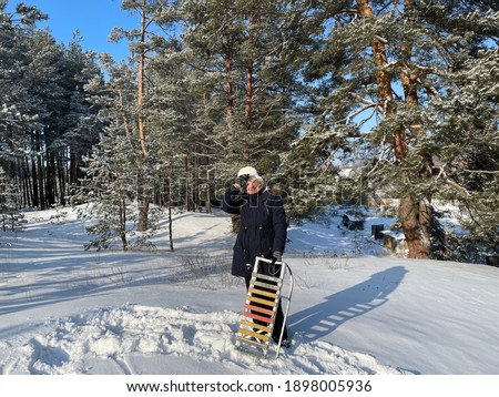 Elderly woman stands with sledges in winter forest