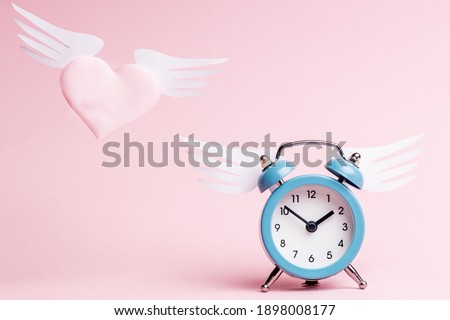 flying heart symbol near alarm clock over pink background. love and romance concept. valentine day greeting card conceptual.