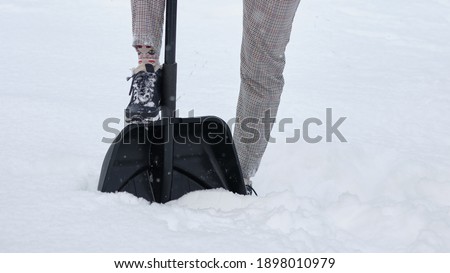 Woman cleaning snow with a shovel close-up view. In the picture, a woman's legs, a shovel and snow