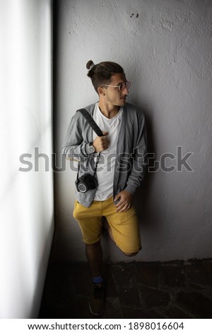 Young stylish photographer holds his camera and leans on a white wall. Photographer concept
