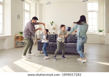 Happy young family with kids enjoying free time on weekend at home. Parents and children dancing and having fun in spacious living-room, celebrating moving into new house or rented apartment Royalty-Free Stock Photo #1898017282