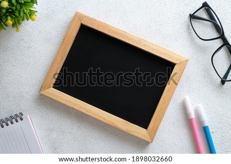 White wooden table with chalkboard, eyeglasses, pen, decorative plants. Top view with copy space, flat lay.