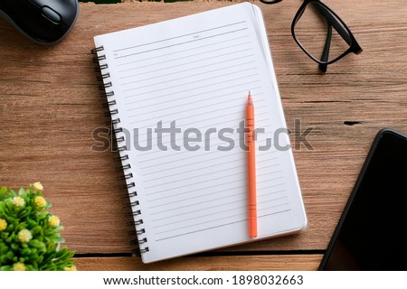 Wooden table with notebook, eyeglasses, pen, decorative plants. Top view of wooden table and stationery with copy space, flat lay.