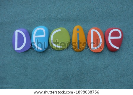 Decide word composed with multi colored stone letters over green sand