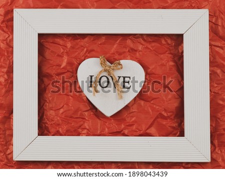 
White wooden heart with the word love lies in the middle in a frame on a red crumpled paper background, close-up top view.
