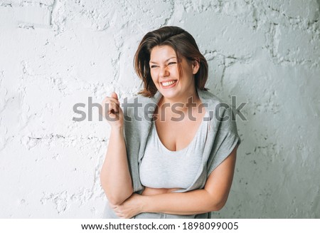 Beautiful happy emotional brunette young woman plus size body positive in comfortable sport wear near the white brick wall Royalty-Free Stock Photo #1898099005