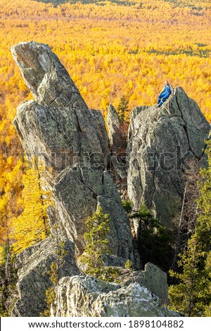 mature tourist posing on the rocks of the mountain round hill on the Alabiya ridge in the Ural mountains on an autumn sunny day.