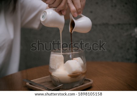 Woman Hands is Pouring Milk into The Cold Lemon Tea or Coffee for Cold Brew Menu. Close-up. Breakfast time. Concept coffee maker pours milk mixed with hot coffee in coffee shop