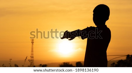 Shadow children exercise on morning of golden sky background, children raise hand for yoga on sunrise, blurred hills and clouds on silhouette wallpaper, lifestyle active of child for relaxing time 