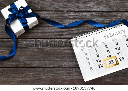 Gift box and calendar with framed date 23 February on wooden background. Defender of the Fatherland Day is a Russian holiday. Flat lay, copy space.