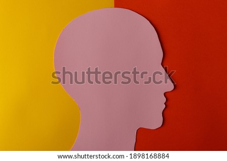 Head silhouette made of paper. Pink paper shaped as a human head with copy space on yellow and red paper background. Minimal concept.