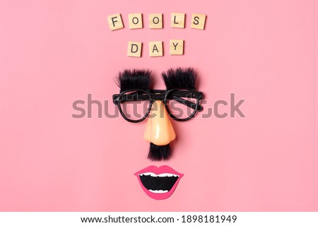 funny face - fake eyeglasses, nose and mustache, text  fools day written on pink background 1st April party Holiday card