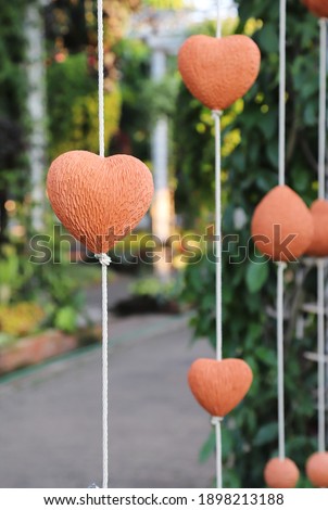 Closeup of brown handmade earthware heart hanging by white rope with garden background in sunny day. Symbol of love and valentine day.  Vertical view.