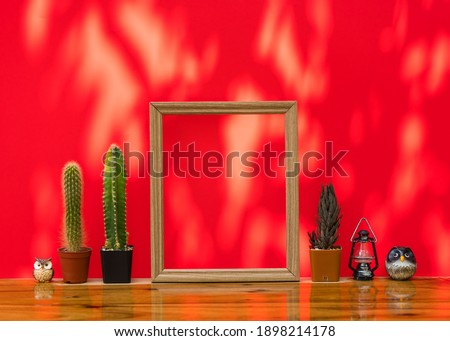 Beautiful  cactus , blank  wooden picture  frame , model  lamp  and   simulated  owl  on  wood  table  with  red  background