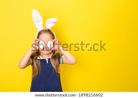 Cute little child girl wearing bunny ears on Easter day. Girl holding painted eggs for easter on yellow background. Banner with copy space