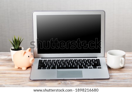 Laptop and pink little piggy bank on a wooden table. online investment