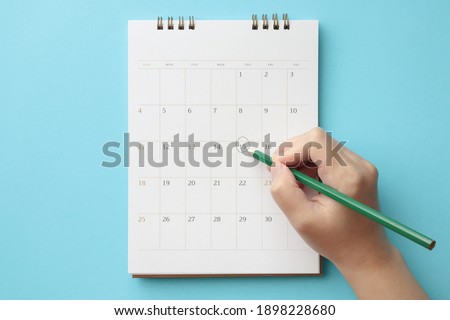 Hand with pencil mark on calendar date on blue background Royalty-Free Stock Photo #1898228680