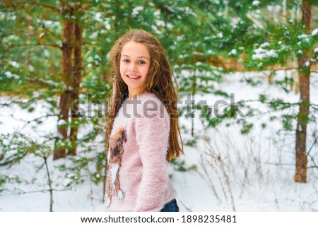 Winter portrait of a little happy girl in a sweater, snow on her hair, snow landscape in the background