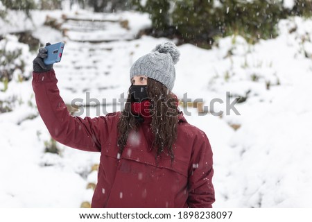 Photo session with a model in the snow, she wears a red coat and a gray hat. It's snowing.
He takes a selfie. He is wearing a mask. Coronavirus, Covid-19
