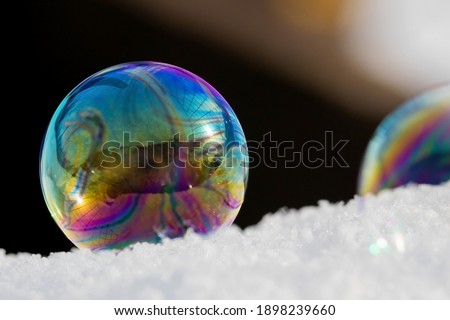 Abstract composition with soap bubble on snow and black background. Rainbow stains and reflections on the sphere