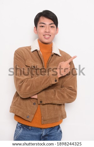 portrait of young man in sweater and brown jacket with blue jeans posing on white background