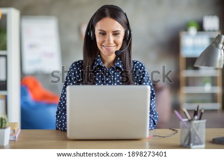 Photo of young beautiful attractive focused smiling positive businesswoman in headphones typing in laptop at office