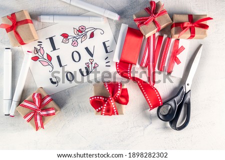 Red ribbons, gifts, scissors, markers next to valentine with words I love you . Preparation for Valentine's Day. Valentine's day concept. Flat lay. Top view