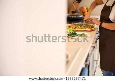 Unrecognized woman cutting pizza on a wooden board in the kitchen. Website banner