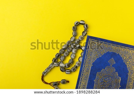 Holy Quran with arabic calligraphy meaning of Al Quran and tasbih or rosary beads on yellow background. Selective focus.