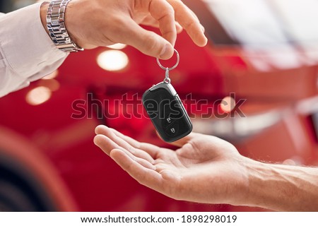 Unrecognizable client receiving keys of rent vehicle from manager against red vehicle in dealership Royalty-Free Stock Photo #1898298019